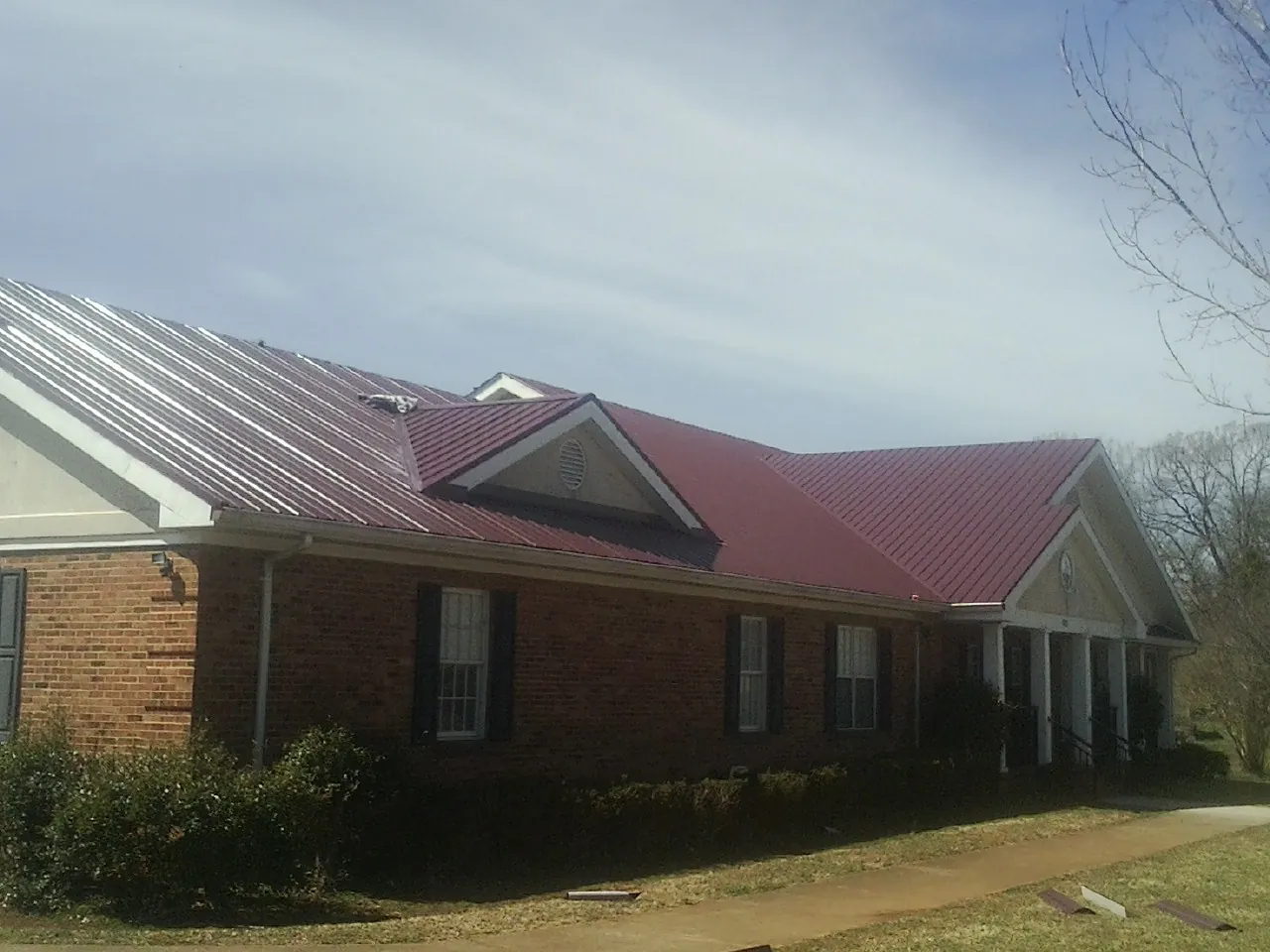 Red metal roof with gabled entries on a long brick building, from a Hail Damage Roof Repair job in Kennerdell