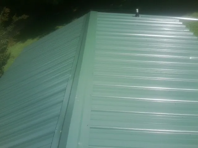 New green metal panels meeting at the ridge of a roof — Flat Roof Repair work by our crew in Kennerdell
