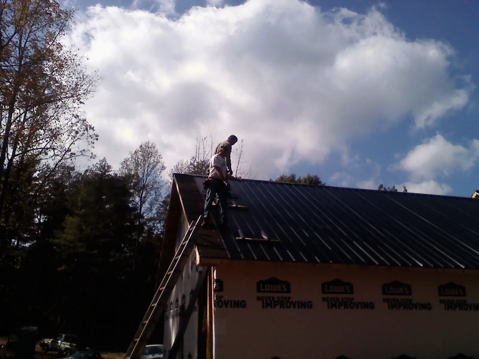 Roofer fastening dark metal panels high against a cloudy sky, from a Roof Inspection job in Kennerdell