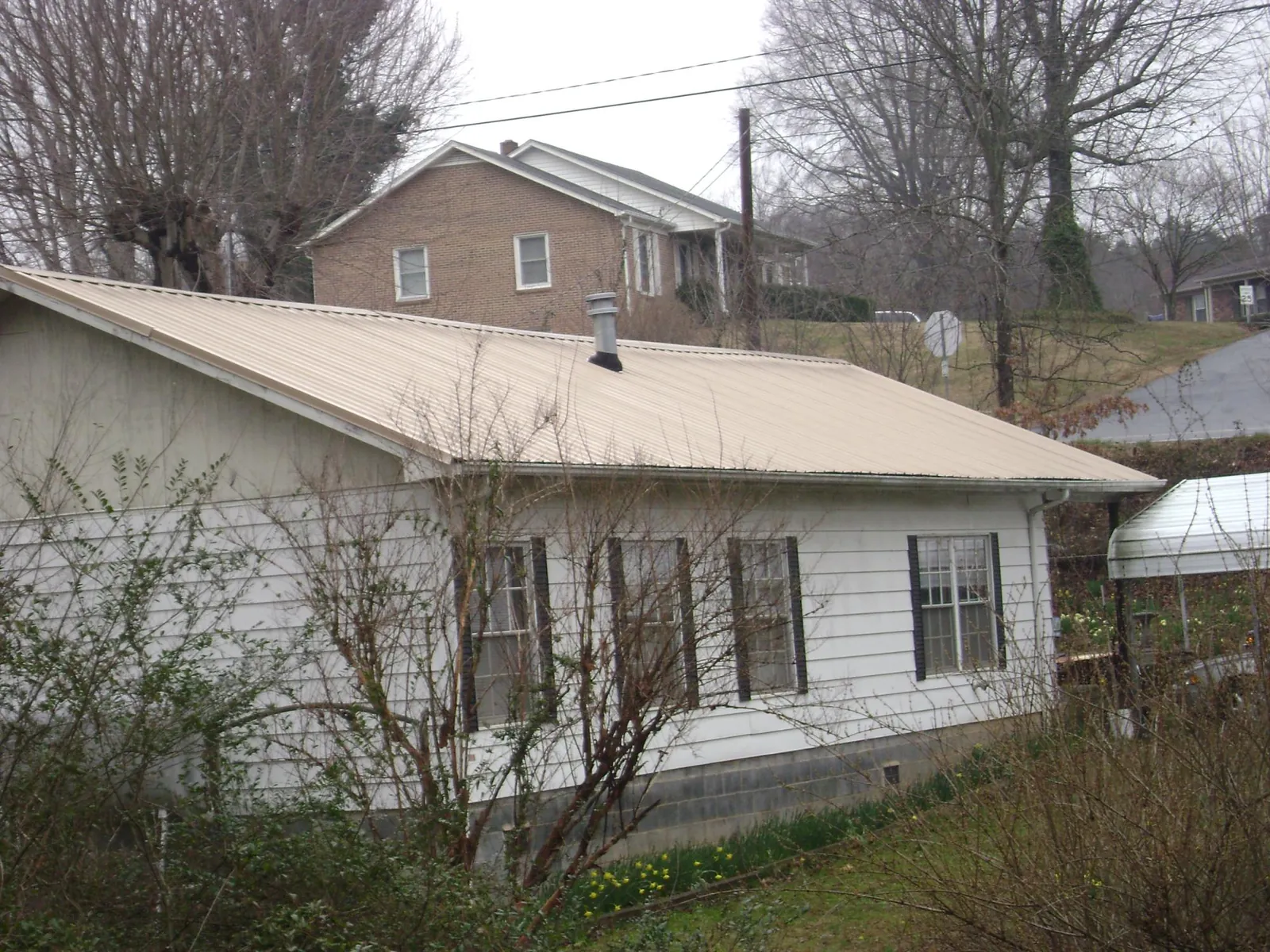 Tan metal roof on a white sided house set into a hillside — Commercial Roofing by Roofing Brothers in Kennerdell
